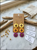 Wildflower Trio Stacked Clay Dangle Earrings featuring yellow sunflower, orange zinnia, and purple aster clay blooms on a handmade card